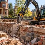 Excavator carefully removing a historic brick and stone foundation near Victorian homes in Toledo’s Old West End.